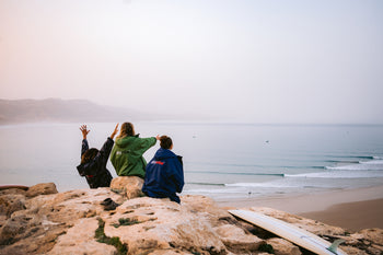 Three people sat on a rock looking at the beach in dryrobes