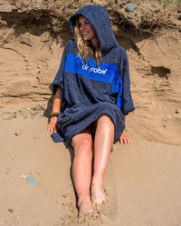 Woman with wet hair sat on the sand on a beach, wearing Organic Towel dryrobe Remix in Navy Royal Blue with hood up