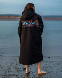 Adult female on beach wearing black blue remix Dryrobe®
