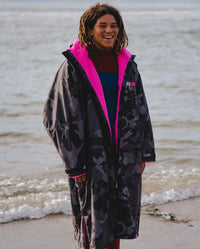 *MALE* dryrobe® Ambassador Siyanda Hewitt standing on a beach, wearing Black Camo Pink dryrobe® Advance Long Sleeve