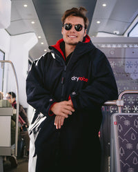 *MALE* Man smiling stood on a bus leaning on a chair, wearing sunglasses and dryrobe Advance Long Sleeve changing robe in Black Red