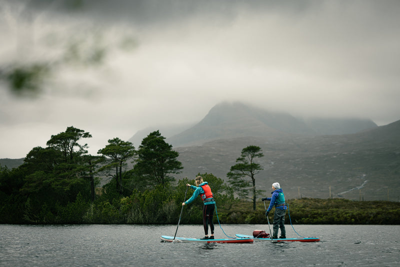 Two people SUPing on a lake with a misty hill in the background