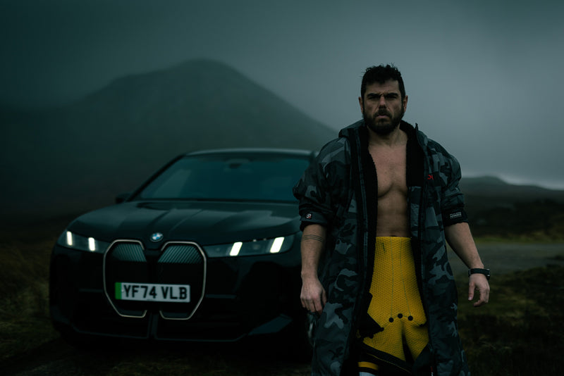 Ross Edgley in a dryrobe stood in front of a mountain and a car 