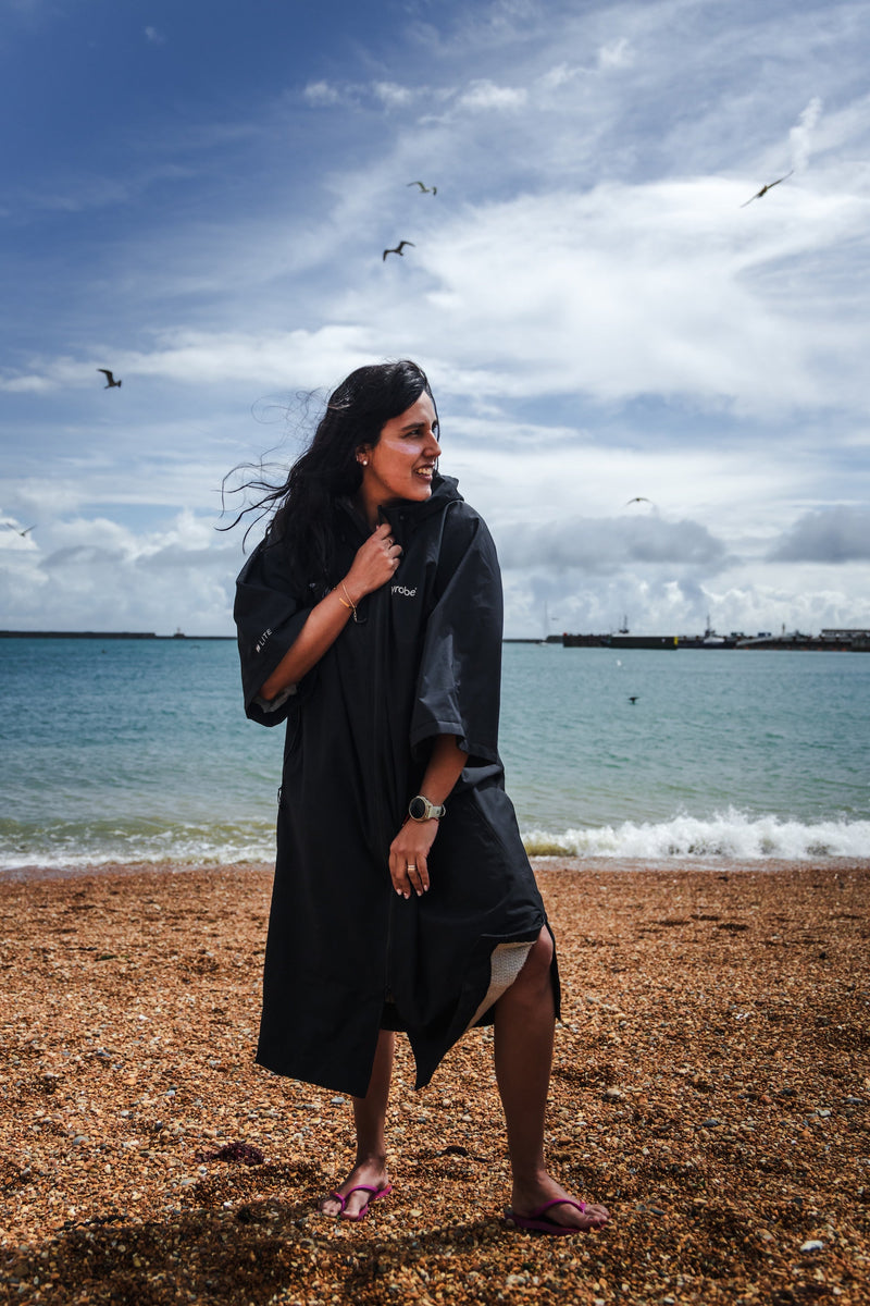 A woman with long dark hair wearing a dryrobe tech lite on the beach with the English Channel in the background
