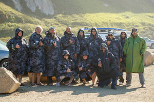 Operation Surf veterans posing for group photo in Black Camo Dryrobe Advances at the beach