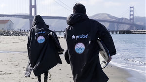 Two surfers walking toward the Golden Gate Bridge wearing black Dryrobe® Advance change robes featuring the City Surf Project patch.