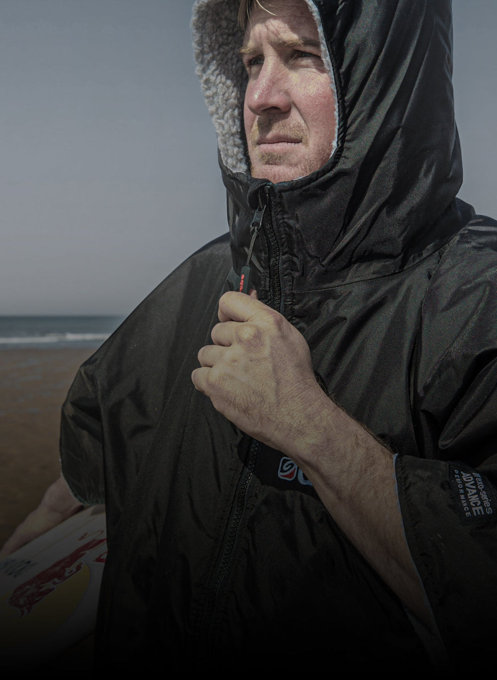 Andrew Cotton wearing short sleeve Dryrobe® holding surfboard on the beach 