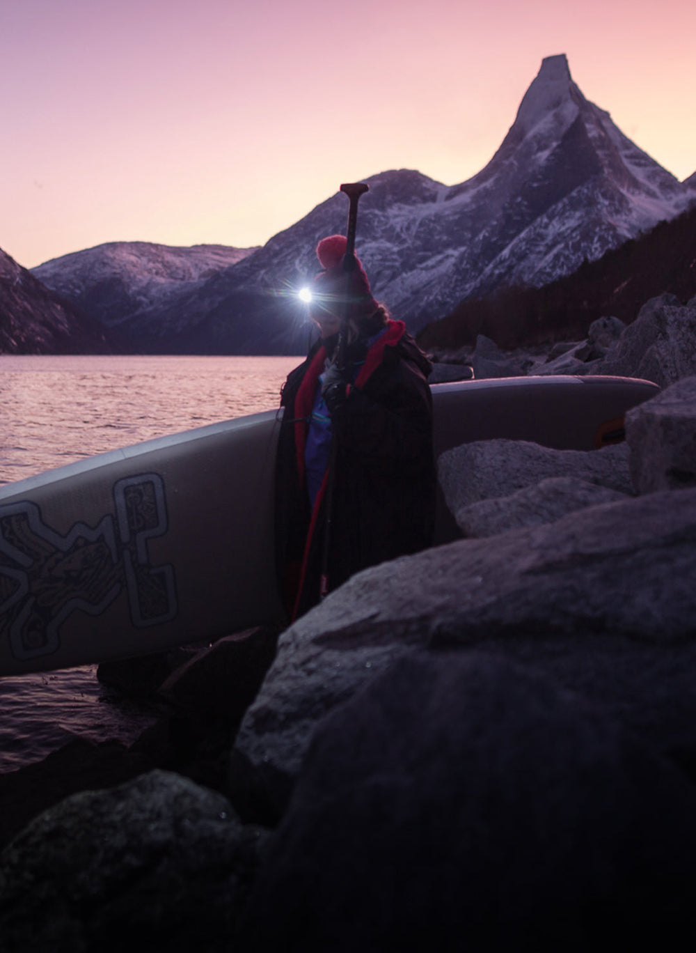 Female adult paddle boarder wearing Dryrobe® walking towards lake with mountains behind 