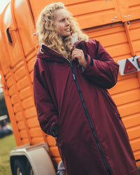 Female standing by horse box wearing AW25 Burgundy Dryrobe® advance long sleeve 