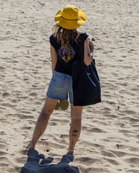 Woman stood on a beach wearing Quick Dry Brimmed Hat holding dryrobe Luxury Tote Bag 