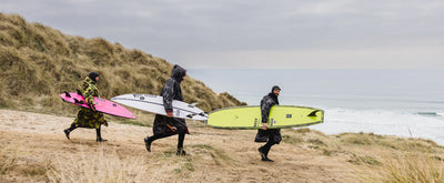 Three surfers wearing Dryrobe Chaning robes walking along a beach path with their surfboards.