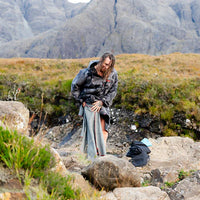 Person in a Dryrobe® changing robe standing on rocky terrain with mountains in the background