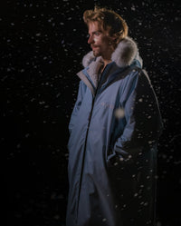 Man stood outside at night in the snow,  wearing dryrobe Advance Long Sleeve Alpine Range change robe in Alpine Ice Blue