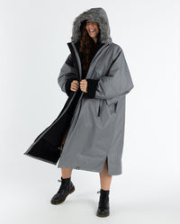 Woman smiling swaying to the side,  wearing dryrobe Advance Long Sleeve Alpine Range change robe in Alpine Graphite with hood up 