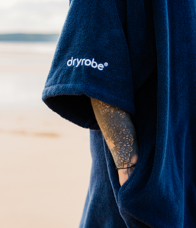 *MALE* Person wearing a blue dryrobe with 'dryrobe' logo on a beach.