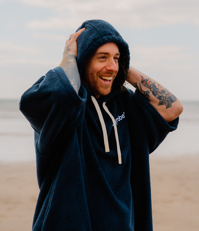 *MALE* Man wearing a navy blue hoodie towel robe with a brand logo on a beach