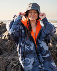 Woman sat on rock on beach, wearing dryrobe Fleece Lined Bucket Hat in Dark Grey and Camo Blue Orange dryrobe Advance