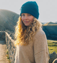 Woman by the coast wearing deep sea blue Dryrobe® Beanie hat 