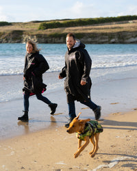 Dog wearing camo black Dogrobe running on the beach