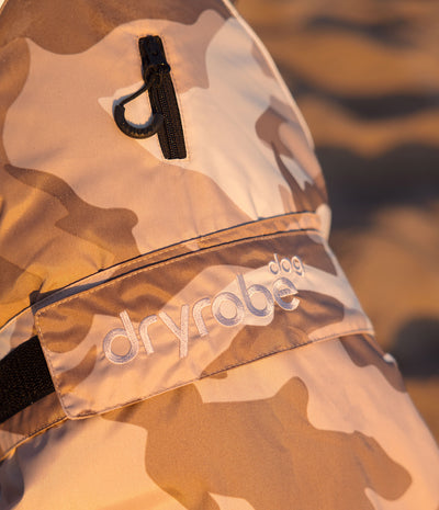 Close-up of a Dryrobe dog jacket in a beige and brown camouflage pattern, featuring a black zipper pocket and a branded elastic strap.
