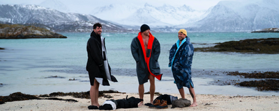 Three people standing on a beach wearing Dryrobes in front of a mountain