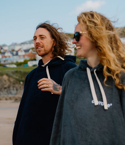 Two people wearing towel robes standing outdoors with a scenic background.