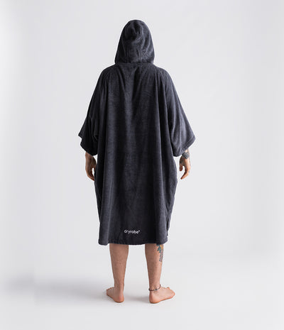 *MALE* Person wearing a dark grey hooded towel robe with 'dryrobe' branding on a white background