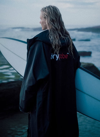 Female surfer wearing Dryrobe® looking out to sea with surfboard 