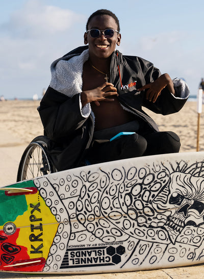 Young man in wheelchair wearing Dryrobe® Adapt with surfboard 