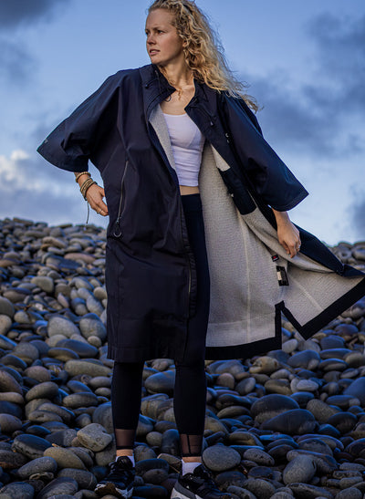Young woman wearing Dryrobe® Lite standing on beach pebbles 