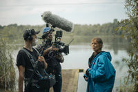 Film crew with camera equipment on a dock by a lake