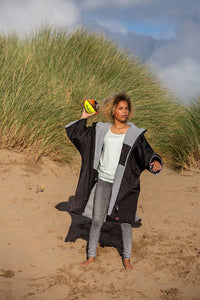 Girl stood on a beach throwing a ball, wearing dryrobe Advance Kids Short Sleeve changing robe in Black Grey 