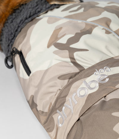 Close-up of a dryrobe dog jacket with a beige and brown camouflage pattern, featuring a gray fleece lining and a silver embroidered dryrobe logo.