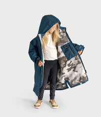 A child wearing a long navy hooded Dryrobe with a gray and white camouflage sherpa lining, shown against a light gray studio background.