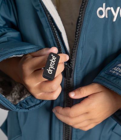 *MALE* A close-up of a person wearing a blue waterproof Dryrobe and holding a small black Dryrobe humidity sensor in their hand.