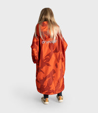 A child viewed from behind wearing a bright orange camouflage hooded Dryrobe with the brand name 'cryroute' printed in white on the back, set against a plain light gray studio background.