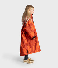 A child viewed from behind wearing a bright orange camouflage hooded Dryrobe with the brand name 'cryroute' printed in white on the back, set against a plain light gray studio background.