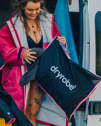Woman in van packing Dryrobe® into Dryrobe® black pink cushion cover 