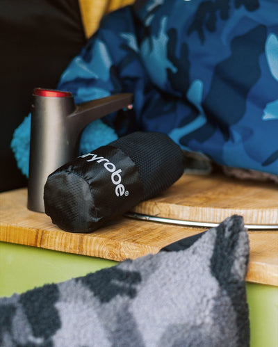Black Dryrobe® microfibre towel product on a wooden surface with a blue camouflage Dryrobe® change robe in the background