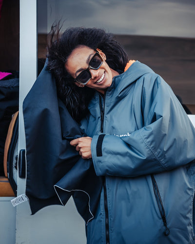 Person wearing a blue Dryrobe® change robe with a hood, smiling outdoors.