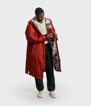 *MALE* A man wearing a red hooded dryrobe Changing robe, with a white logo on the chest, photographed against a light gray studio background.