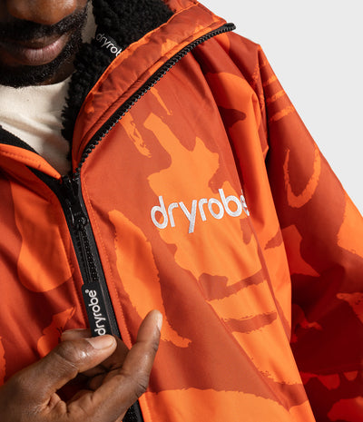 *MALE* Close-up of a person wearing an orange Dryrobe jacket with a tonal orange camouflage pattern, black zipper, and white logo on the chest.