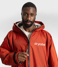 *MALE* A man wearing a red hooded dryrobe Changing robe, with a white logo on the chest, photographed against a light gray studio background.