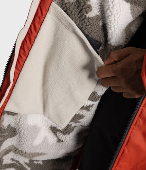 *MALE* Close-up of a person wearing a bright red technical Changing robe, pulling a black zipper on the chest while showing a branded cuff label that reads 'MAXI-SERIES ADVANCE PERFORMANCE'.