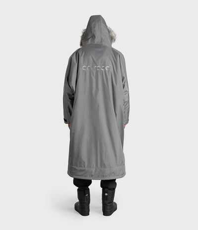 *MALE* A person shown from the back wearing a long gray hooded Dryrobe with a faux-fur trimmed hood and a subtle white 'dryrobe' logo on the upper back, paired with black pants and black boots against a light gray studio background.