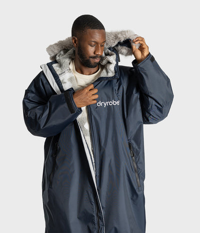 *MALE* A man wearing a navy blue Dryrobe hooded with a gray faux-fur trimmed hood, posing against a light gray studio background.
