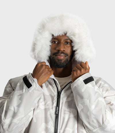 *MALE* A man wearing a white faux-fur lined hooded Dryrobe with a light gray camouflage pattern, holding the hood up against a plain light gray background.