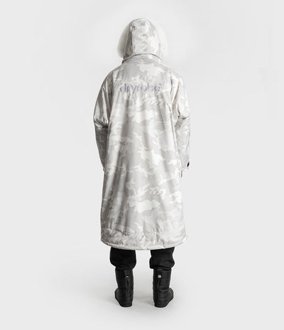 *MALE* A person shown from the back wearing a hooded Dryrobe with a light gray and white camouflage pattern and a subtle tonal logo on the upper back, paired with black pants and black boots against a plain light gray studio background.