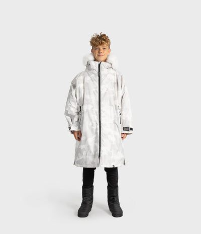 *MALE* A child model wearing a long white hooded Dryrobe with a subtle gray camo pattern, black pants, and black boots, standing against a light gray studio background.