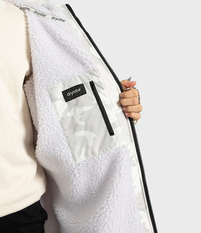 *MALE* Close-up of a person wearing a white sherpa-lined Dryrobe, holding the zipper open to show the interior pocket with a black Dryobe label.